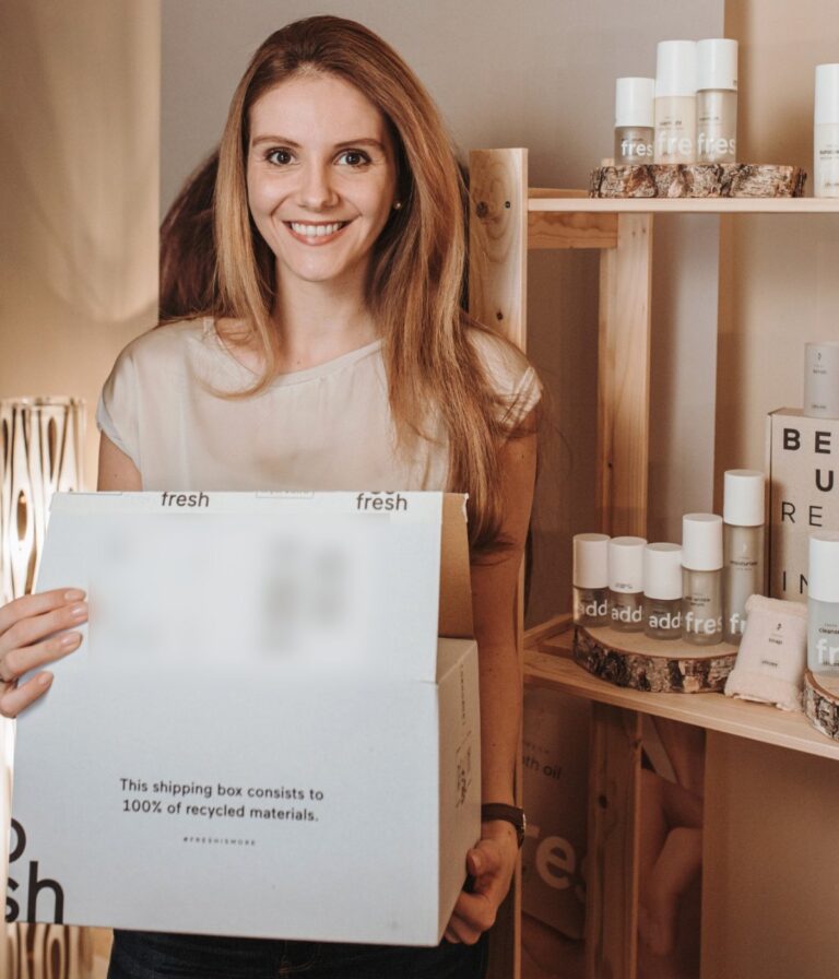Lea, independent RINGANA partner, holding a RINGANA shipping box next to a shelf of RINGANA products