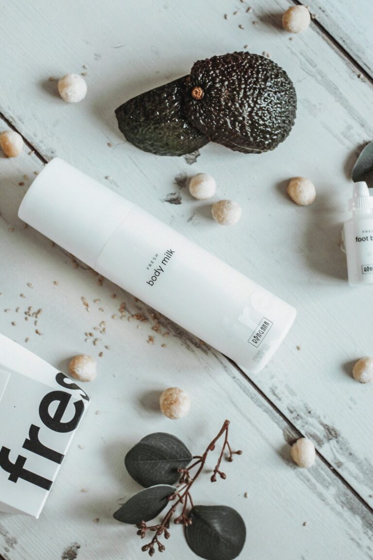 RINGANA FRESH body milk on a white wooden table with macadamia nuts and avocado