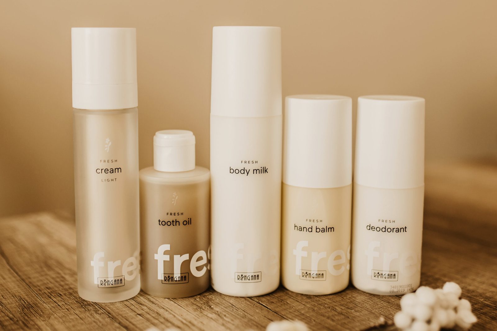 RINGANA FRESH cream, tooth oil, body milk, hand balm and deodorant lined up on wood